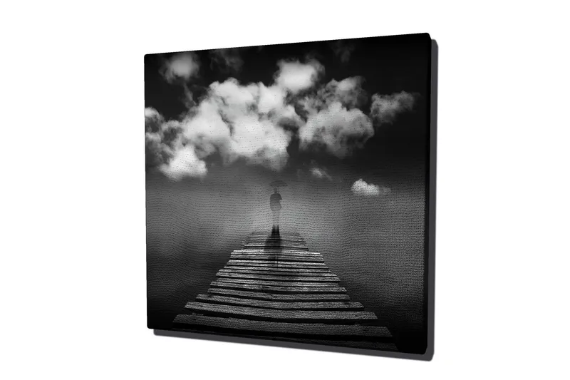 Canvas-taulu 45x45 cm - Yksinäinen hahmo sateenvarjon kanssa puisella sillalla dramaattisten pilvien alla, Musta / Valkoinen / Harmaa