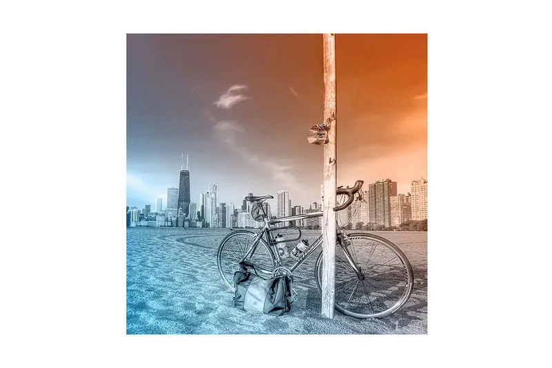 Canvas-taulu 45x45 cm - Polkupyörä nojaa tolppaan, taustalla kaupungin siluetti, Sininen / oranssi