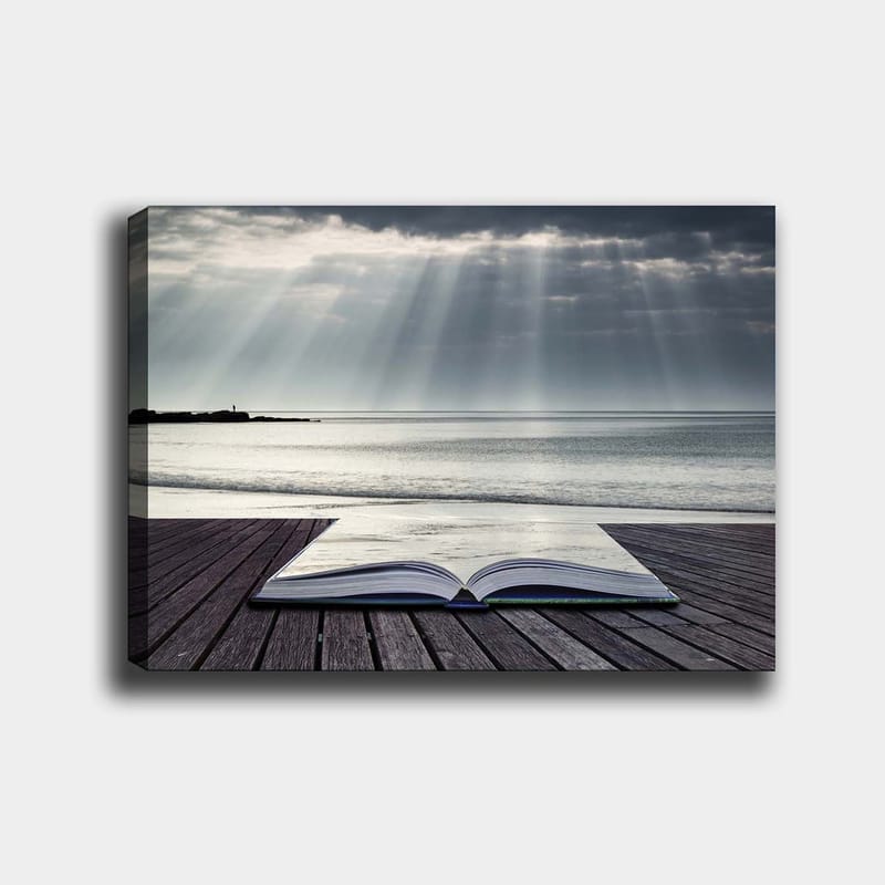 Canvas taulu 70x100 cm - Avoin kirja puisella laiturilla meren rannalla, pilvisen taivaan pehmeiden valonsäteiden ympäröimänä, Harmaa / Sininen / Valkoinen