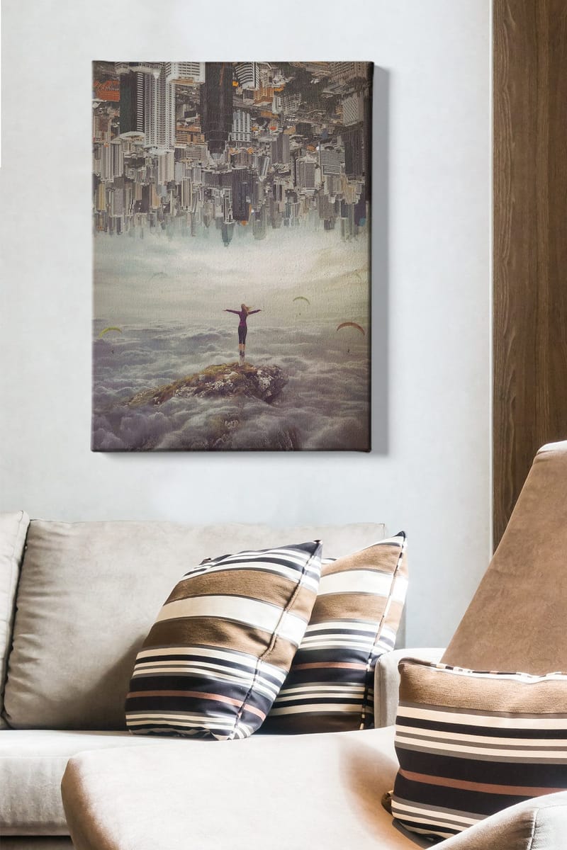 Canvas taulu 70x100 cm - Henkilö seisoo kädet ojennettuina kalliolla pilvien yläpuolella, taustalla ylösalaisin oleva kaupunki - Harmaa / Beige / Tummansininen - Sisustustuotteet - Taulu & taide - Canvas-taulu