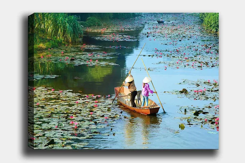 Canvas taulu 70x100 cm - Kaksi ihmistä melomassa veneellä järvellä, jossa on lumpeita ja kukkia, Vihreä / Vaaleanpunainen / Sininen