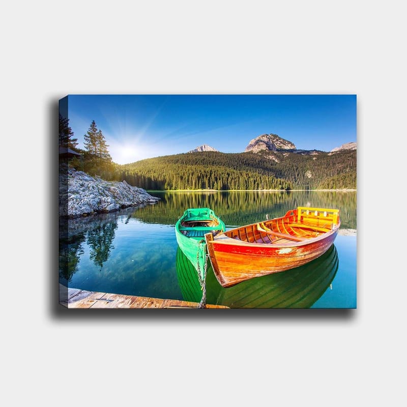 Canvas taulu 70x100 cm - Kaksi värikästä venettä makaa paikallaan peilimäisellä järvellä rehevien vuorten ympäröimänä, Vihreä / Oranssi / Sininen