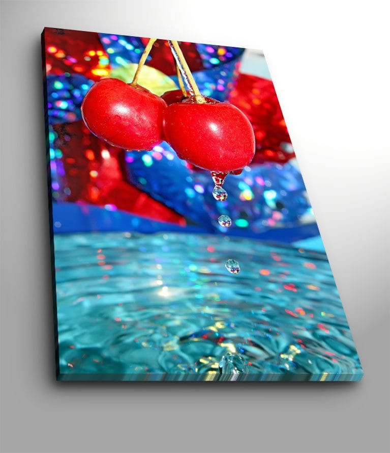 Canvas taulu 70x100 cm - Kaksi punaista kirsikkaa roikkuu vedenpinnan yllä ja pisarat putoavat alas, Punainen / Sininen / Turkoosi