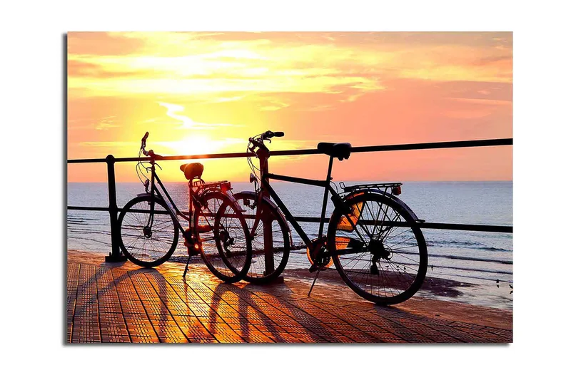 Canvas taulu 70x100 cm - Kaksi polkupyörää laiturilla auringonlaskun aikaan meren yllä, Oranssi / Musta / Keltainen
