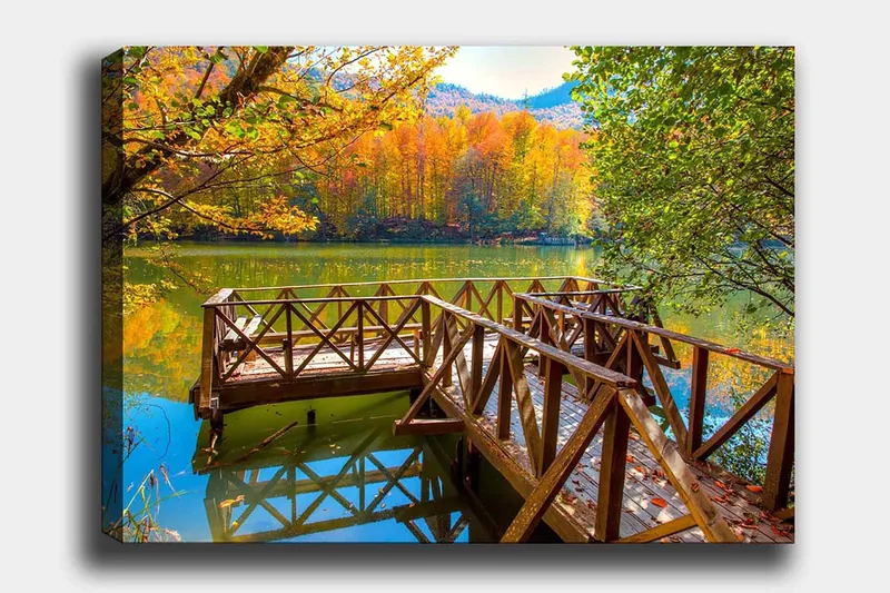 Canvas taulu 70x100 cm - Kaunis laituri peilimäisen järven rannalla syksyn väristen puiden ympäröimänä, Kulta / Vihreä / Ruskea