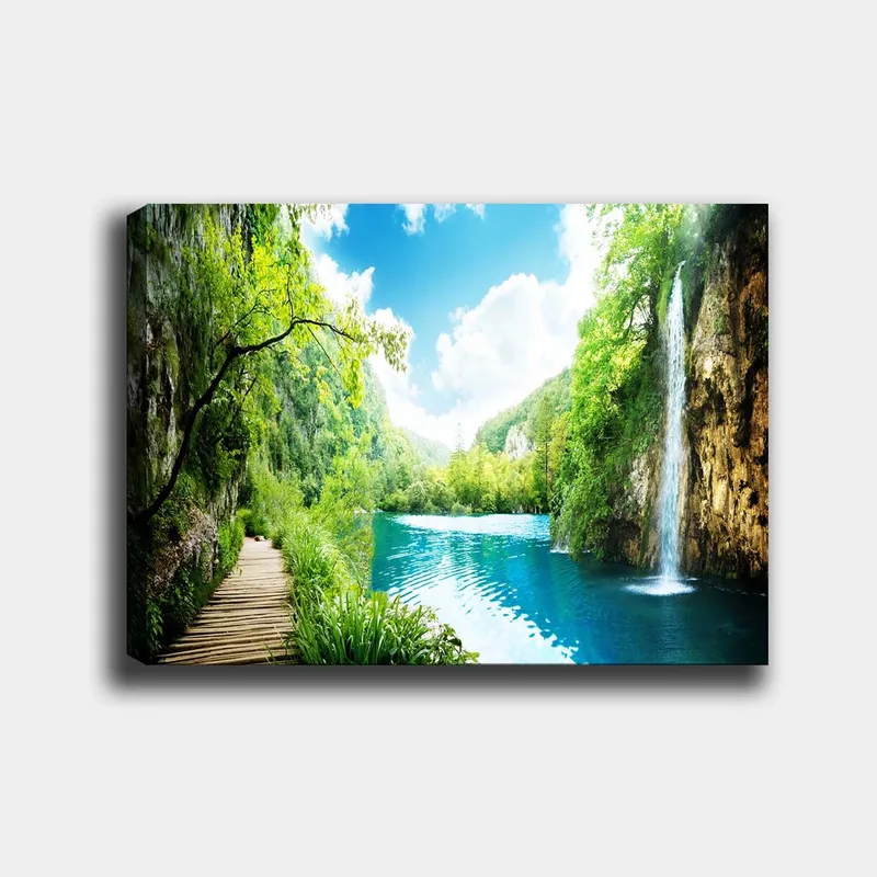 Canvas taulu 70x100 cm - Kaunis luontomaisema vesiputouksella, joka virtaa kirkkaaseen, siniseen järveen rehevän vehreyden ja vuorten ympäröimänä, Vihreä / Sininen