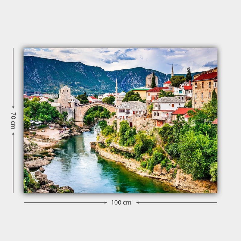 Canvas taulu 70x100 cm - Kaunis näkymä historiallisesta joen ylittävästä sillasta, jota ympäröivät viehättävät talot ja rehevä vehreys. - Vihreä / Sininen / Punainen - Sisustustuotteet - Taulu & taide - Canvas-taulu