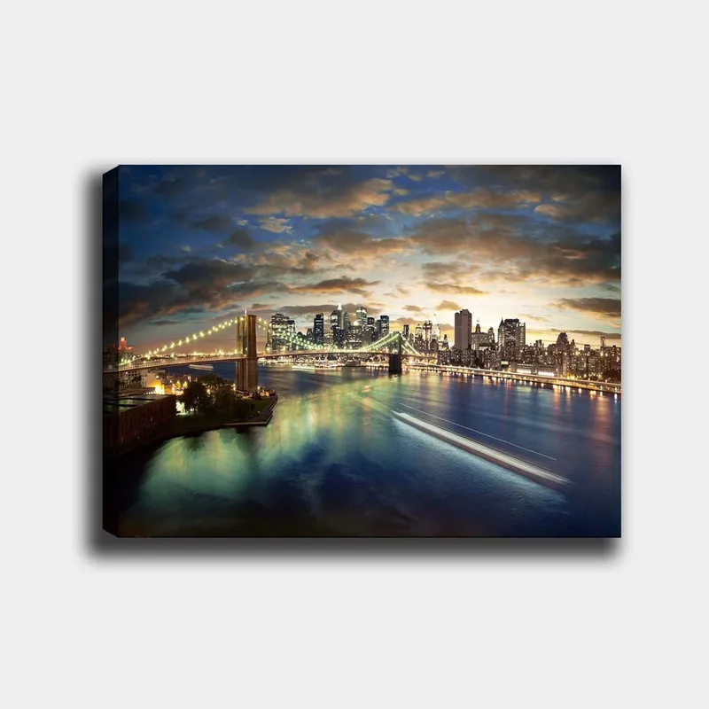 Canvas taulu 70x100 cm - Kaunis näkymä kaupunkiin ja sillalle, joka ylittää kimmeltävän joen hämärässä, Sininen / Vihreä / Oranssi