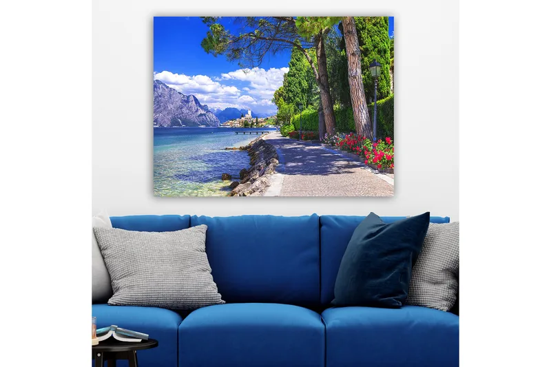 Canvas taulu 70x100 cm - Kaunis rantakatu puiden ja kukkien ympäröimänä järven rannalla, vuorten ympäröimänä ja taustalla viehättävä kaupunki - Sininen / Vihreä / Punainen - Sisustustuotteet - Taulu & taide - Canvas-taulu