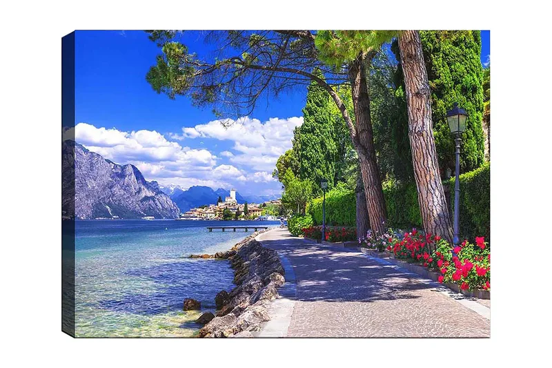 Canvas taulu 70x100 cm - Kaunis rantakatu puiden ja kukkien ympäröimänä järven rannalla, vuorten ympäröimänä ja taustalla viehättävä kaupunki, Sininen / Vihreä / Punainen