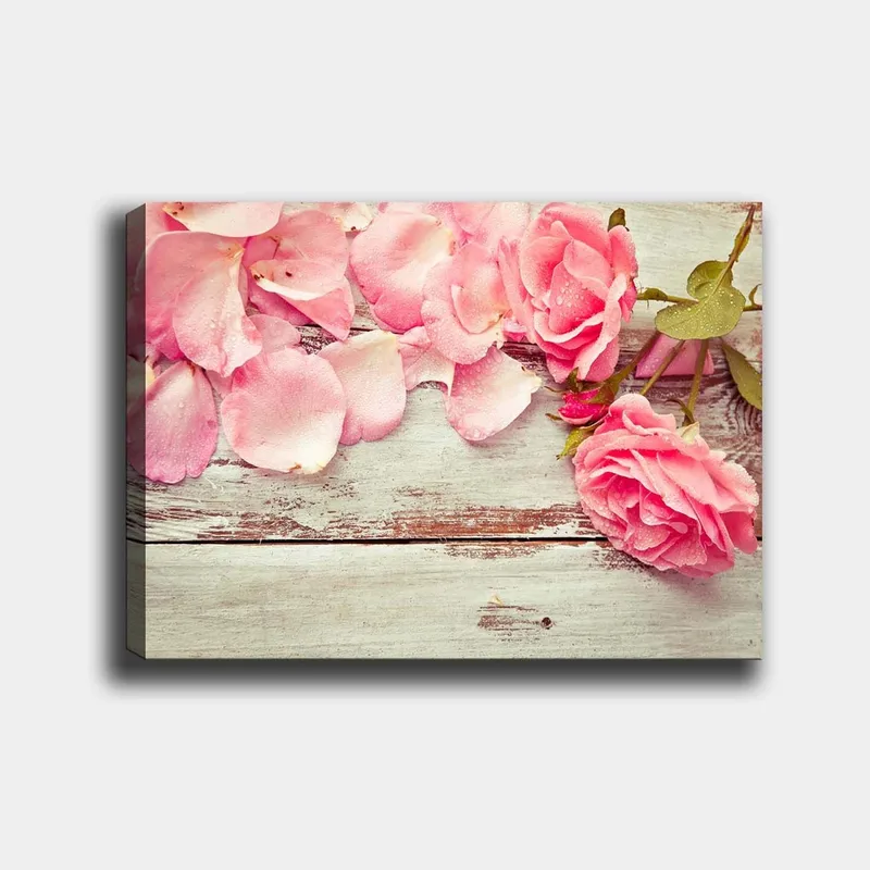 Canvas taulu 70x100 cm - Kaunis vaaleanpunaisten ruusujen ja ruusun terälehdistä koostuva sommitelma puupinnalla, Vaaleanpunainen / Vihreä / Ruskea