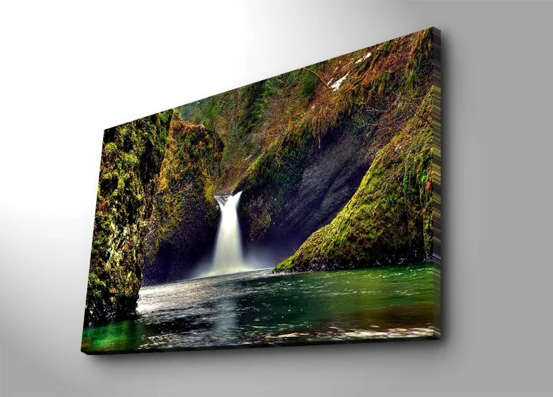 Canvas taulu 70x100 cm - Kaunis vesiputous virtaa alas vihreiden kallioiden välistä luonnonkauniissa ympäristössä, Vihreä / Sininen / Ruskea