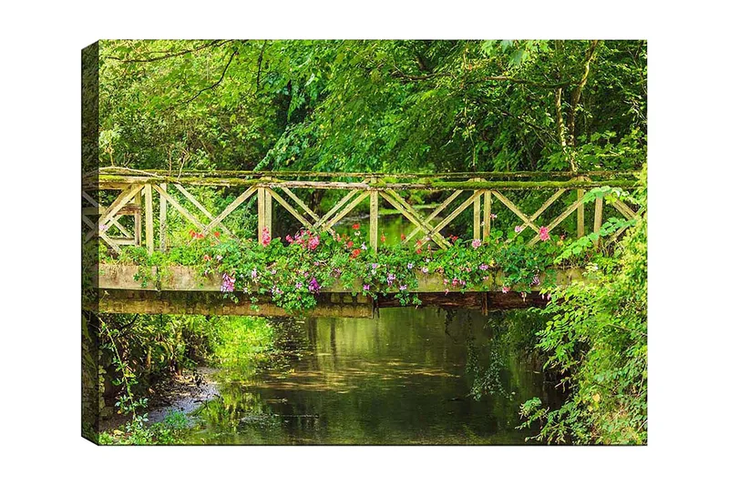 Canvas taulu 70x100 cm - Kaunis puinen silta, jota ympäröi vehreys ja kukat tyynen veden äärellä, Vihreä / Vaaleanpunainen / Ruskea