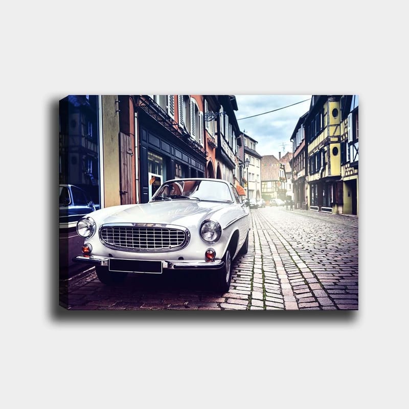 Canvas taulu 70x100 cm - Klassinen valkoinen auto pysäköitynä viehättävälle, vanhanaikaiselle kadulle historiallisten rakennusten ympäröimänä, Valkoinen / Musta / Harmaa