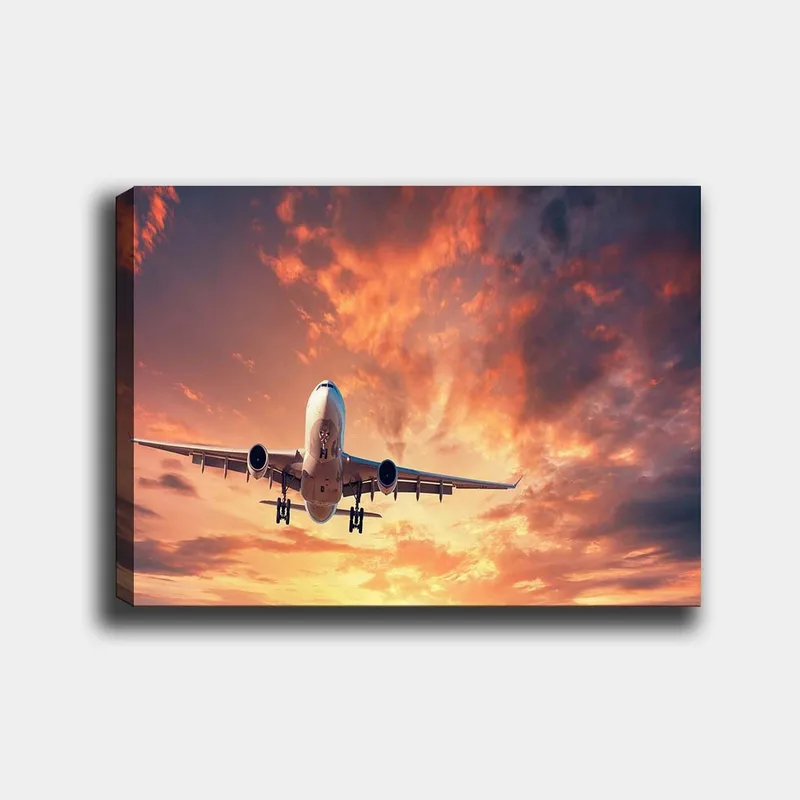Canvas taulu 70x100 cm - Lentokoneen laskeutuminen dramaattista auringonlaskua ja värikkäitä pilviä vasten, Oranssi / Violetti / Sininen