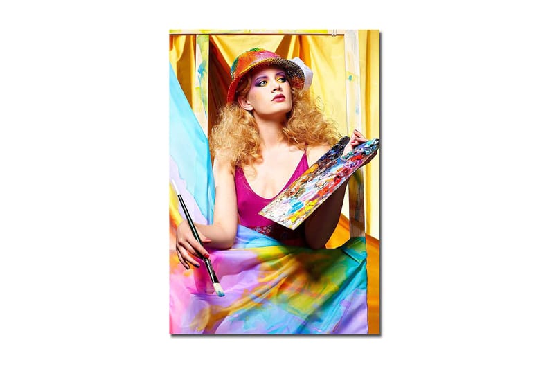 Canvas taulu 70x100 cm - Luova nainen maalaa paletti kädessään, värikkäiden kankaiden ympäröimänä, Vaaleanpunainen / Sininen / Keltainen