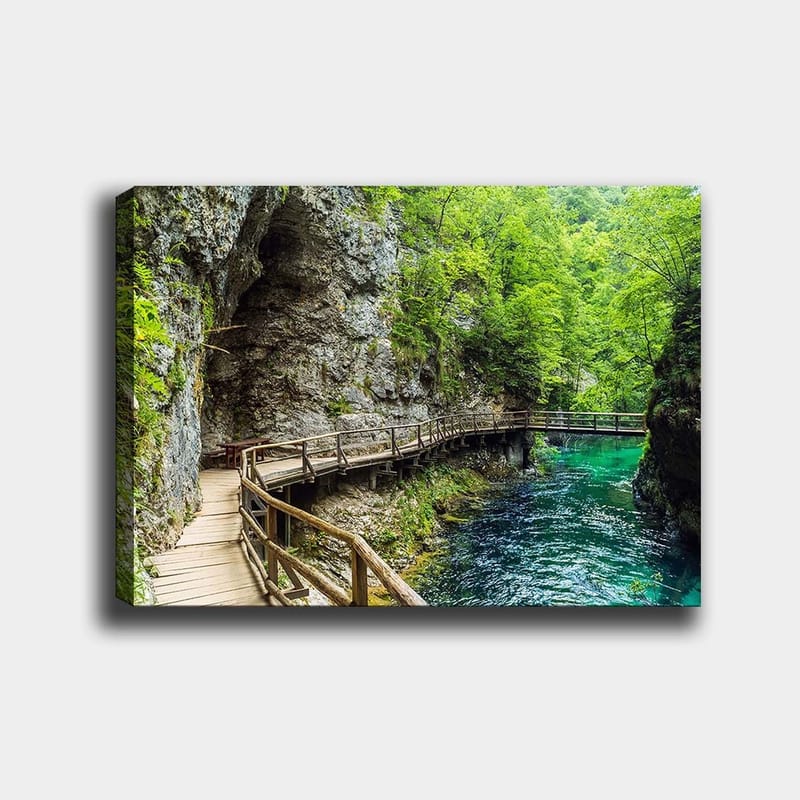 Canvas taulu 70x100 cm - Maisemanäkymä puisesta sillasta, joka mutkittelee rehevän rotkon läpi kirkkaan, turkoosin joen varrella, Vihreä / Turkoosi / Harmaa