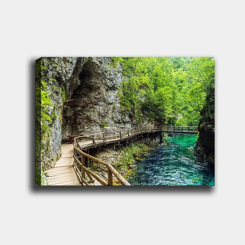 Canvas taulu 70x100 cm - Maisemanäkymä puisesta sillasta, joka mutkittelee rehevän rotkon läpi kirkkaan, turkoosin joen varrella, Vihreä / Turkoosi / Harmaa