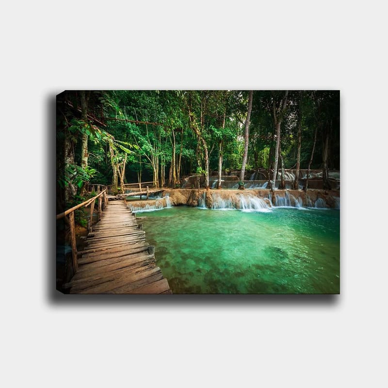 Canvas taulu 70x100 cm - Rauhallinen ja luonnonkaunis paikka, jossa puinen silta johtaa kirkkaan, turkoosin vesiputousaltaan yli rehevän vehreyden ympäröimänä, Turkoosi / Vihreä / Ruskea