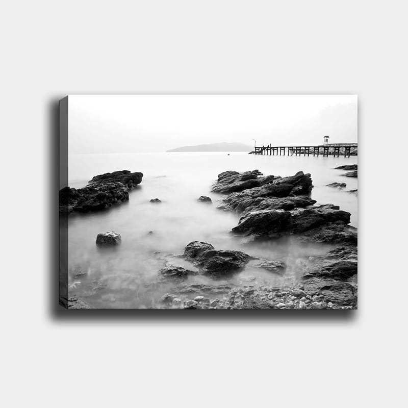 Canvas taulu 70x100 cm - Rauhallinen rannikkomaisema kallioilla ja laituri kaukaisuudessa, Musta / Valkoinen / Harmaa