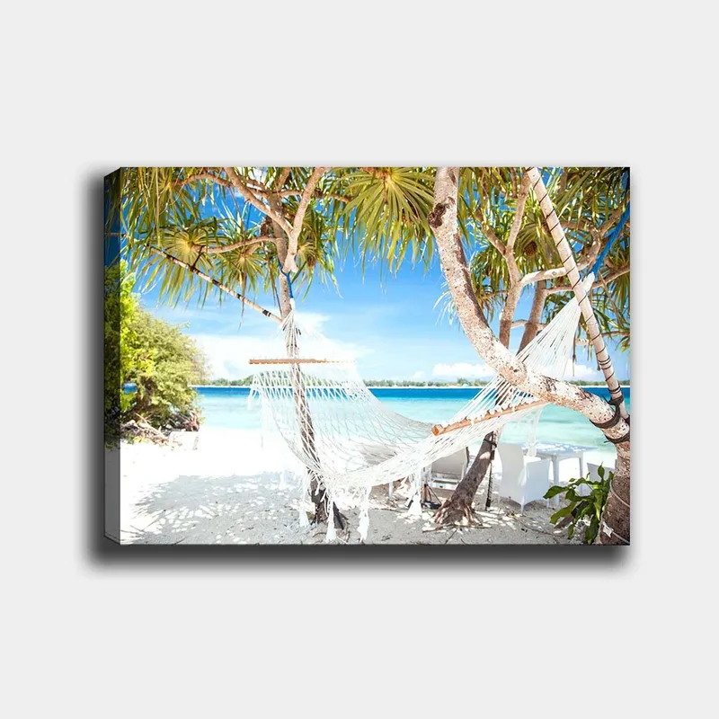 Canvas taulu 70x100 cm - Rentouttava riippumatto palmujen välissä rannalla, jossa on turkoosi vesi ja kirkas sininen taivas, Valkoinen / Sininen / Vihreä