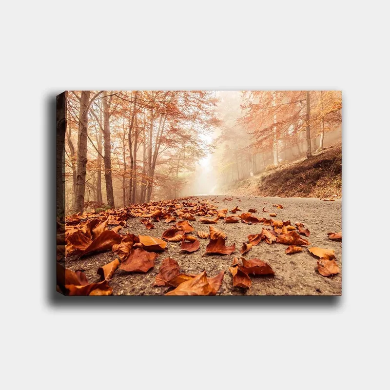 Canvas taulu 70x100 cm - Syksyinen tie, jota reunustavat pudonneet, ruskeat lehdet puiden alla, joissa on kultaisia ja oransseja lehtiä, Oranssi / Ruskea