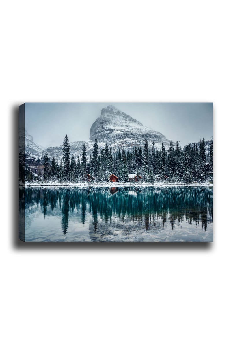 Canvas taulu 70x100 cm - Talvimaisema lumipeitteisillä vuorilla ja peilimäisellä järvellä, jota ympäröivät kuusimetsät ja punaiset mökit, Tummanvihreä / Sininen / Valkoinen