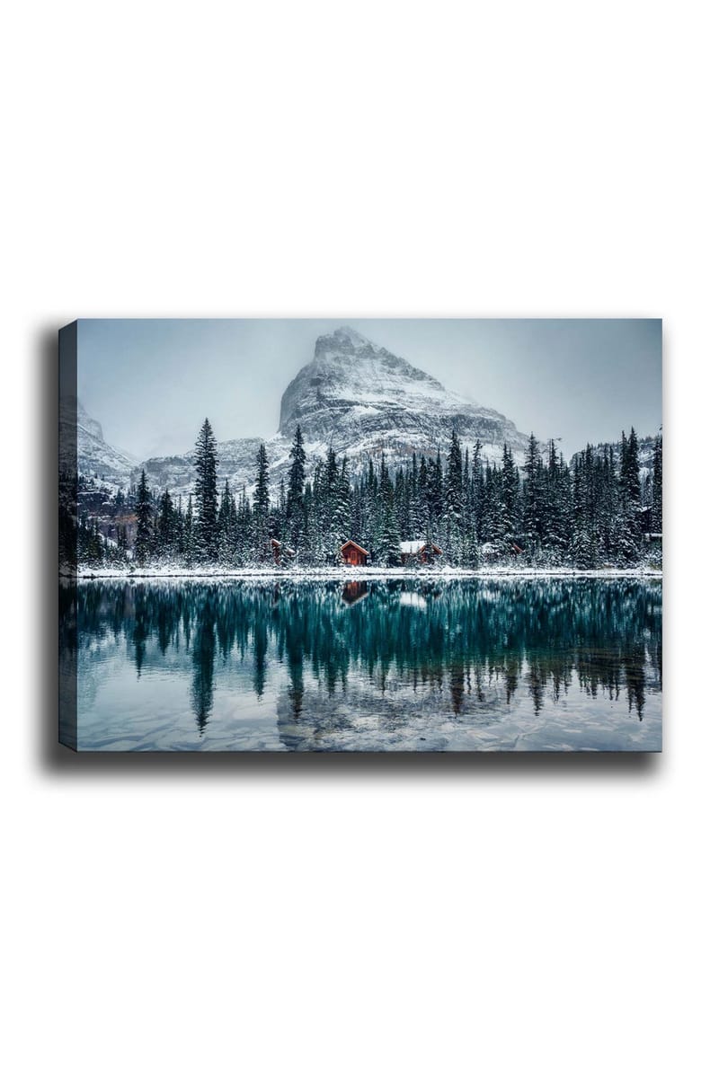 Canvas taulu 70x100 cm - Talvimaisema lumipeitteisillä vuorilla ja peilimäisellä järvellä, jota ympäröivät kuusimetsät ja punaiset mökit, Tummanvihreä / Sininen / Valkoinen