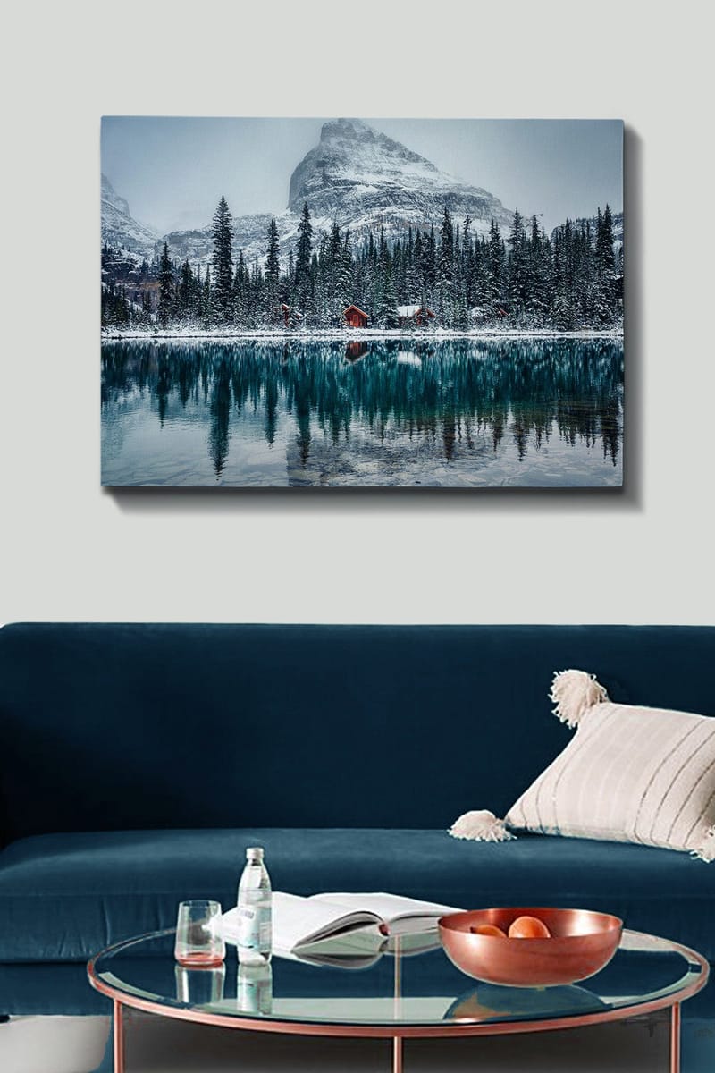 Canvas taulu 70x100 cm - Talvimaisema lumipeitteisillä vuorilla ja peilimäisellä järvellä, jota ympäröivät kuusimetsät ja punaiset mökit - Tummanvihreä / Sininen / Valkoinen - Sisustustuotteet - Taulu & taide - Canvas-taulu