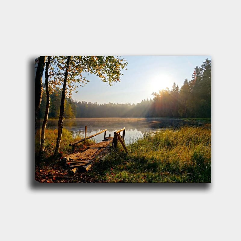 Canvas taulu 70x100 cm - Tyyni järvi ja puinen silta, jota ympäröivät rehevät puut ja aamuauringon säteet, Vihreä / Ruskea / Keltainen