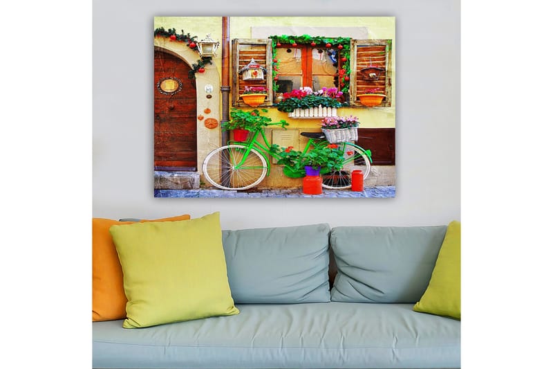 Canvas taulu 70x100 cm - Värikäs, kukilla ja ruukuilla koristeltu polkupyörä viehättävän ikkunoilla ja koristeilla varustetun seinän edessä - Vihreä / Vaaleanpunainen / Oranssi - Sisustustuotteet - Taulu & taide - Canvas-taulu