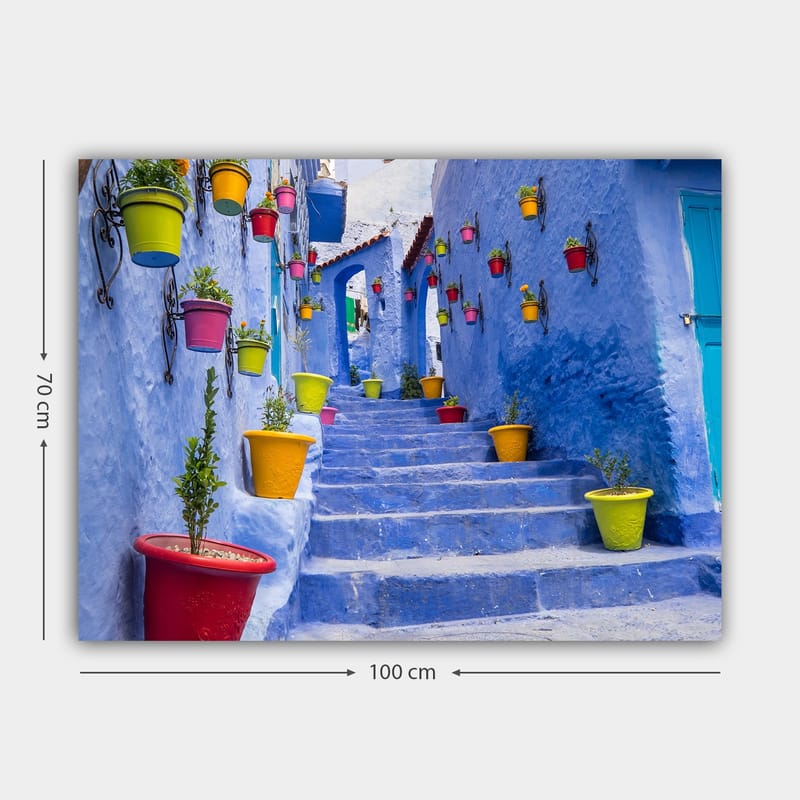 Canvas taulu 70x100 cm - Värikäs portaikko kukkaruukkujen ympäröimänä viehättävässä, sinisessä kaupunkiympäristössä - Sininen / Keltainen / Punainen - Sisustustuotteet - Taulu & taide - Canvas-taulu