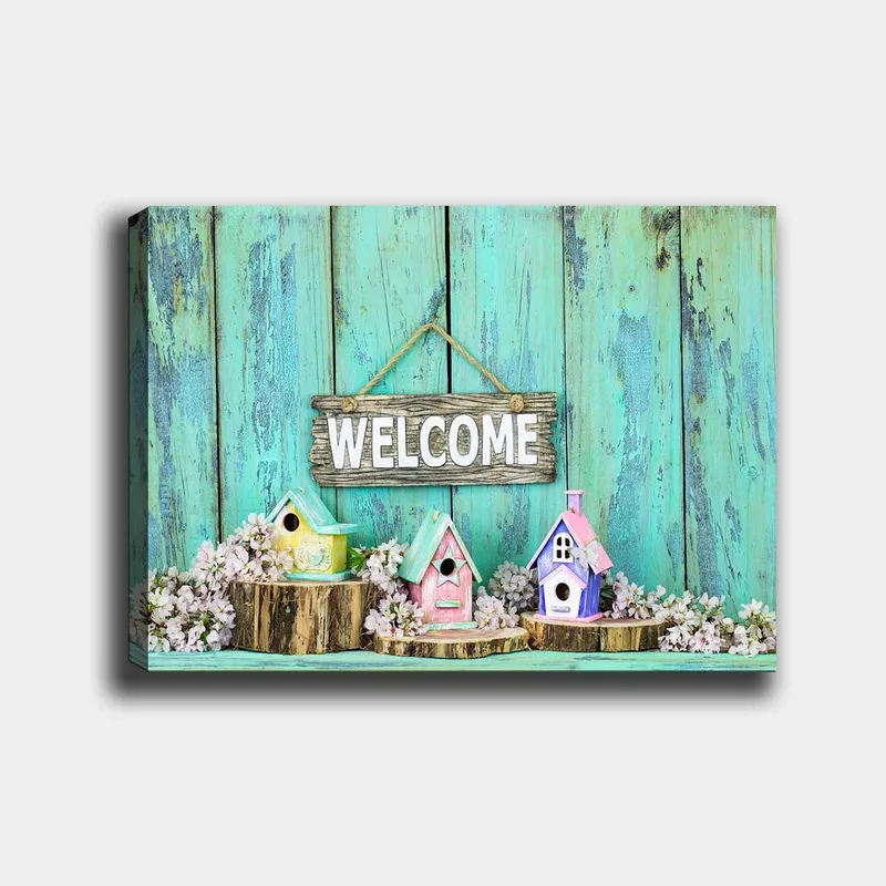 Canvas taulu 70x100 cm - Värikkäitä linnunpönttöjä viihtyisässä ympäristössä puisella kyltillä, Turkoosi / Vaaleanpunainen / Keltainen