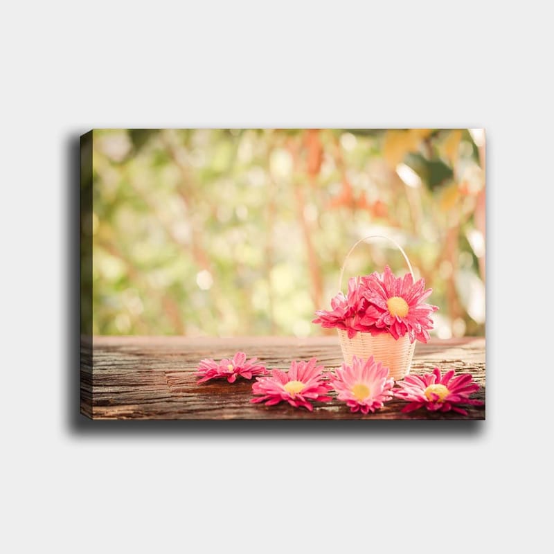 Canvas taulu 70x100 cm - Vaaleanpunaisilla kukilla täytetty kori puupinnalla, Vaaleanpunainen / Keltainen / Ruskea