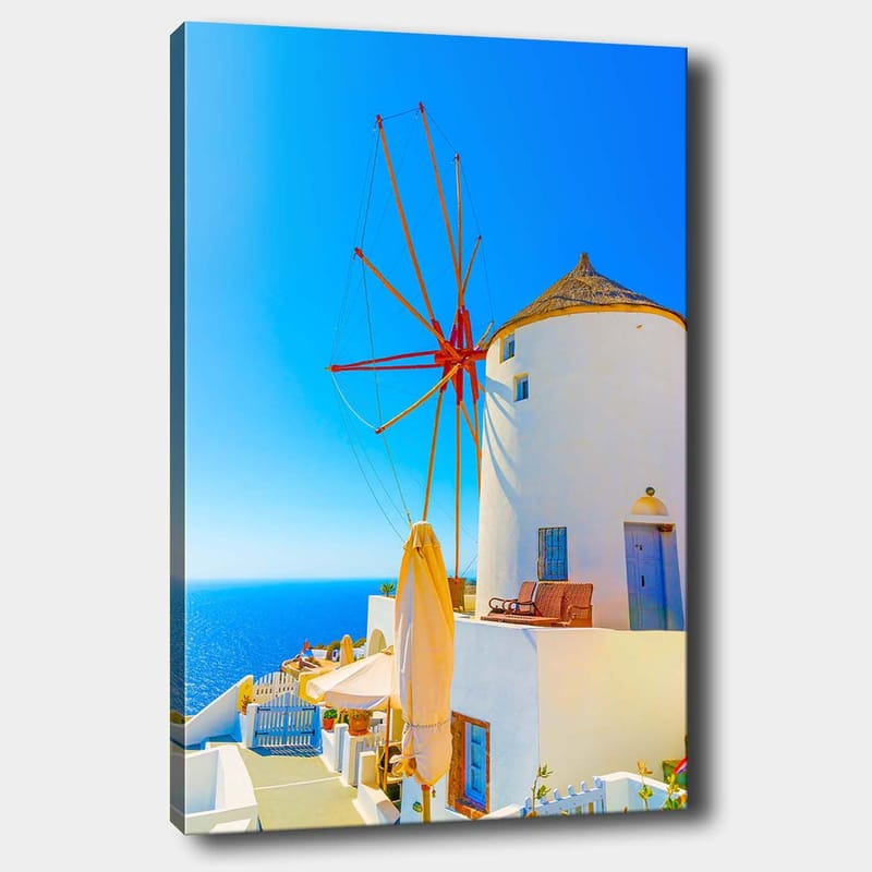 Canvas taulu 70x100 cm - Valkoinen tuulimylly punaisella roottorilla kalliolla meren rannalla, kirkkaan sinisen taivaan ja meren ympäröimänä, Valkoinen / Punainen / Sininen