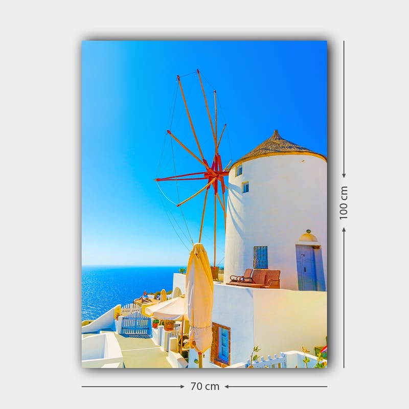 Canvas taulu 70x100 cm - Valkoinen tuulimylly punaisella roottorilla kalliolla meren rannalla, kirkkaan sinisen taivaan ja meren ympäröimänä - Valkoinen / Punainen / Sininen - Sisustustuotteet - Taulu & taide - Canvas-taulu