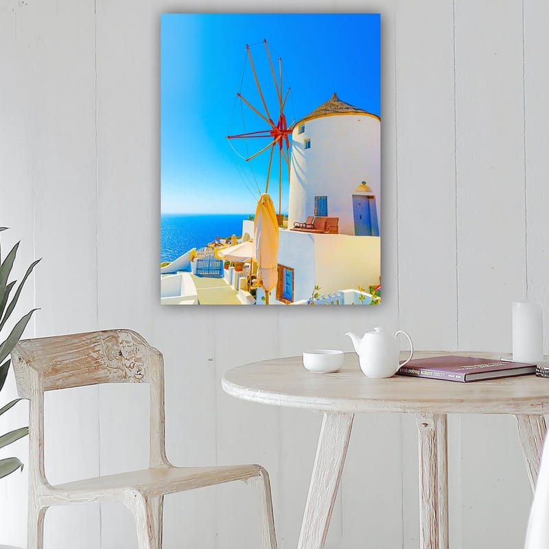Canvas taulu 70x100 cm - Valkoinen tuulimylly punaisella roottorilla kalliolla meren rannalla, kirkkaan sinisen taivaan ja meren ympäröimänä - Valkoinen / Punainen / Sininen - Sisustustuotteet - Taulu & taide - Canvas-taulu
