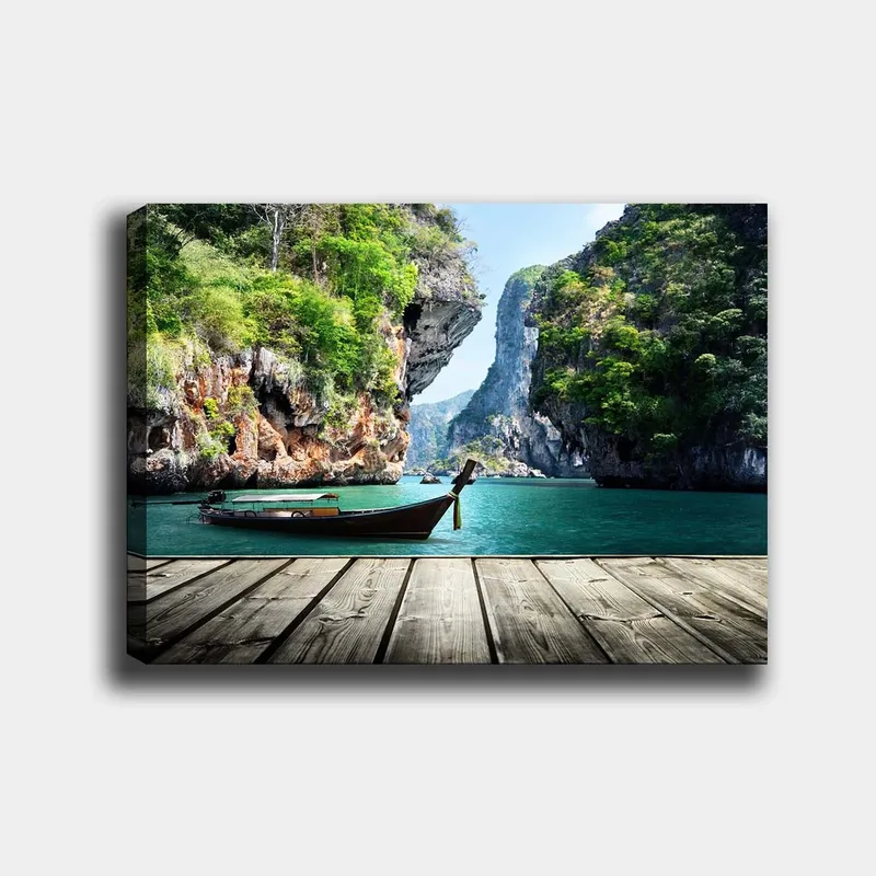 Canvas taulu 70x100 cm - Vene makaa paikallaan kallioisella rannalla rehevien vuorten ja kirkkaan veden ympäröimänä, Vihreä / Sininen / Ruskea