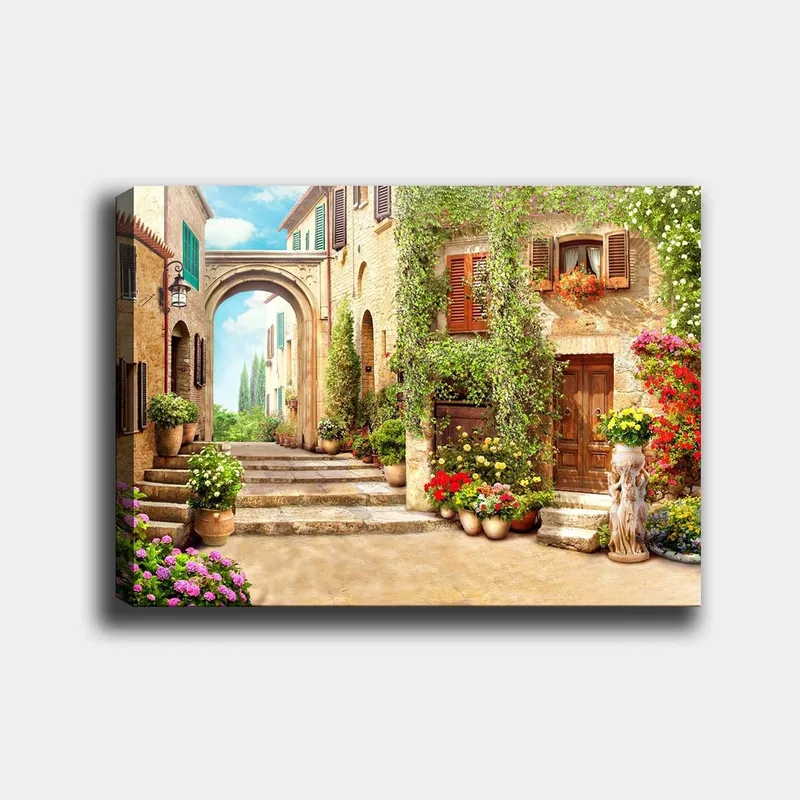 Canvas taulu 70x100 cm - Viehättävä katu kukkien ja vehreyden keskellä viehättävässä kylämäisessä ympäristössä, Vihreä / Keltainen / Vaaleanpunainen