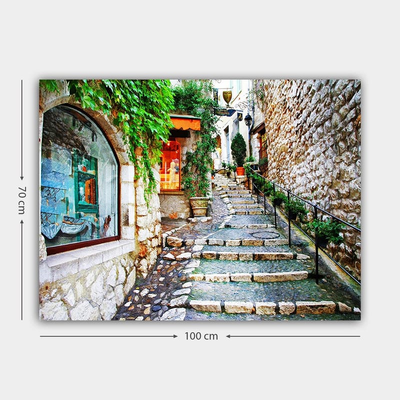 Canvas taulu 70x100 cm - Viehättävä kuja, jonka varrella on kiviä ja vehreyttä, ja jota ympäröivät historialliset rakennukset. - Vihreä / Beige / Oranssi - Sisustustuotteet - Taulu & taide - Canvas-taulu