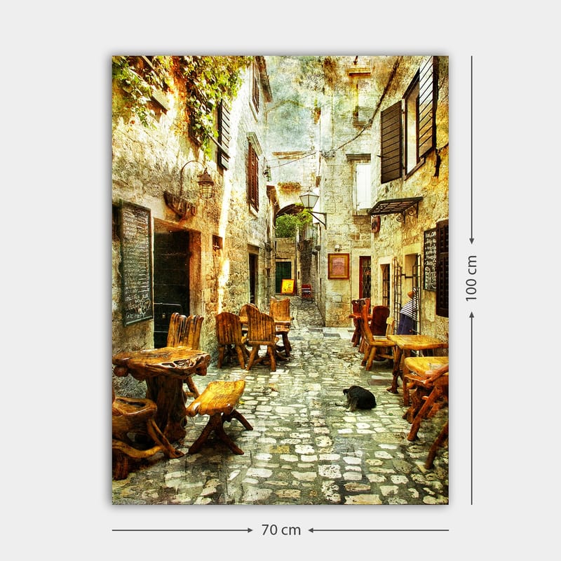 Canvas taulu 70x100 cm - Viehättävä kuja, jossa on puisia pöytiä ja tuoleja, vanhojen kivitalojen ympäröimänä - Ruskea / Harmaa / Vihreä - Sisustustuotteet - Taulu & taide - Canvas-taulu