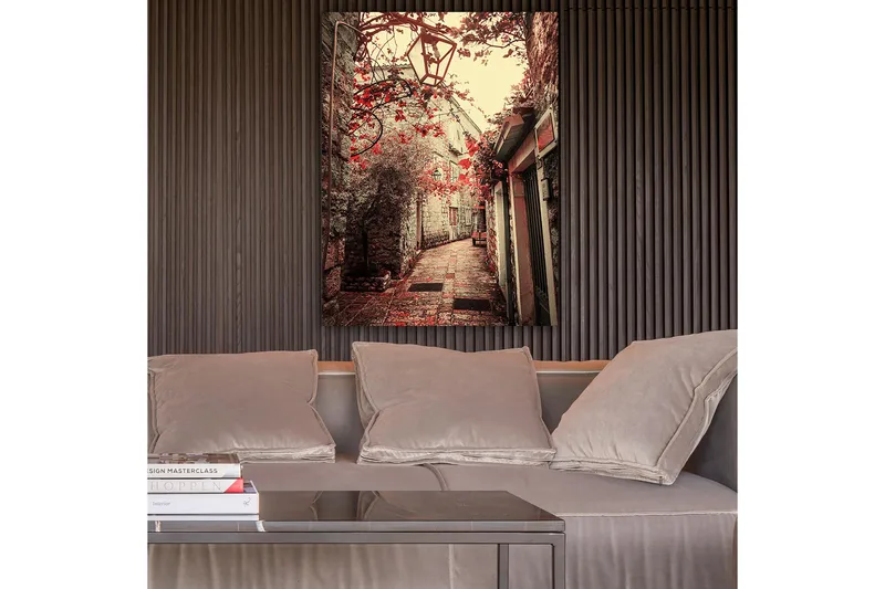 Canvas taulu 70x100 cm - Viehättävä kuja, jota reunustavat vanhat rakennukset ja punaisen sävyiset kukat, Punainen / Beige