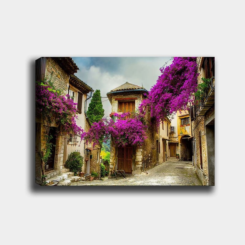 Canvas taulu 70x100 cm - Viehättävä kuja, jota ympäröivät värikkäät kukat viehättävässä kylämiljöössä - Violetti / Vihreä / Beige - Sisustustuotteet - Taulu & taide - Canvas-taulu