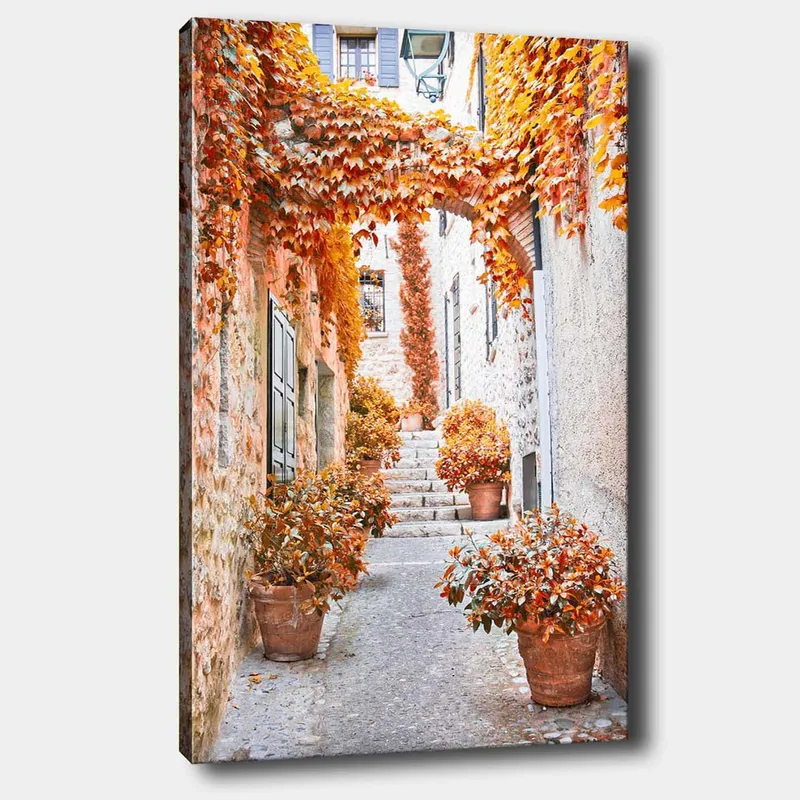 Canvas taulu 70x100 cm - Viehättävä kuja, jota ympäröivät värikkäät syksyn lehdet ja ruukkukasvit, Oranssi / Ruskea / Keltainen