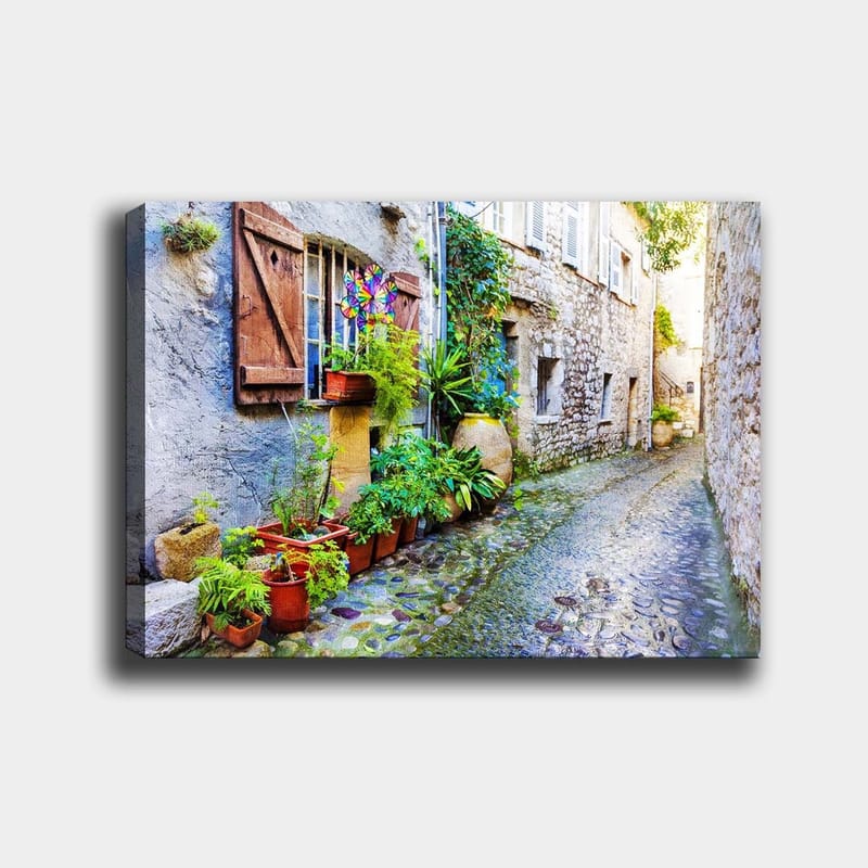 Canvas taulu 70x100 cm - Viehättävä kuja kivitaloineen ja kukkaruukkuineen luo eloisan tunnelman, Vihreä / Sininen / Beige