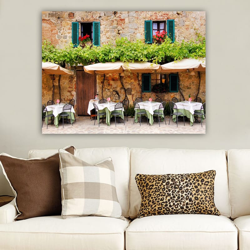 Canvas taulu 70x100 cm - Viehättävä ulkoruokailutila valkoisine pöydineen ja vihreine pöytäliinoineen vanhan kivitalon edessä, jossa on tummanvihreät ikkunaluukut - Tummanvihreä / Valkoinen / Tiilenpunainen - Sisustustuotteet - Taulu & taide - Canvas-taulu