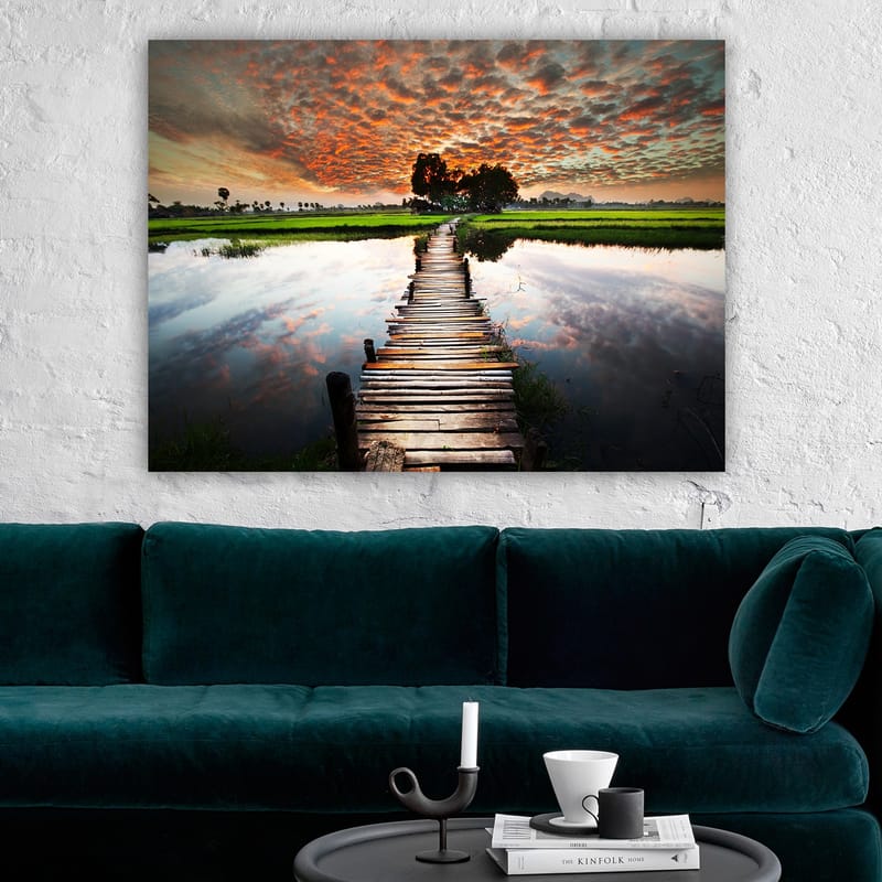 Canvas taulu 70x100 cm - Puinen silta, joka ylittää peilimäisen veden pinnan, rehevän vehreyden ja dramaattisen auringonlaskun ympäröimänä - Oranssi / Vihreä / Sininen - Sisustustuotteet - Taulu & taide - Canvas-taulu