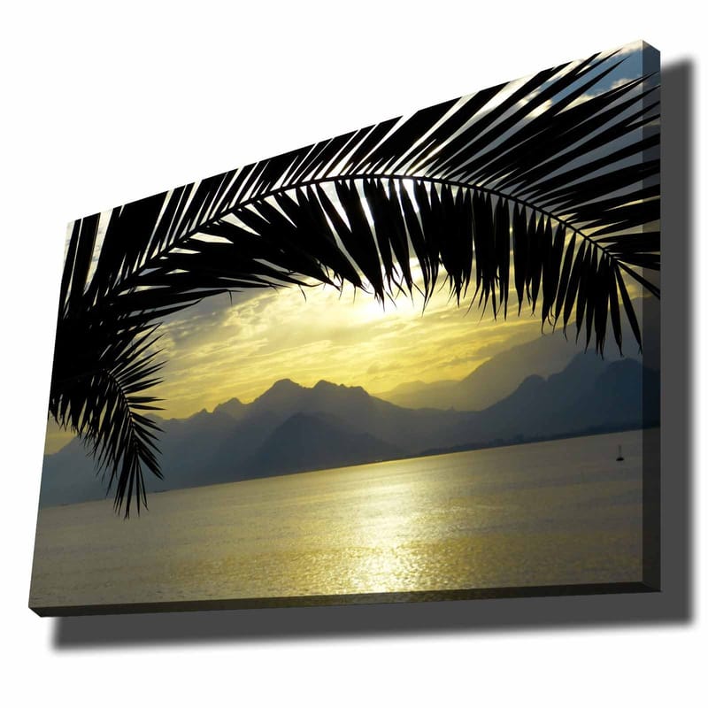 Canvas taulu 70x100 cm - Palmujen siluetti kultaista auringonlaskua vasten vuorten ja meren yllä, Musta / Kulta / Harmaa