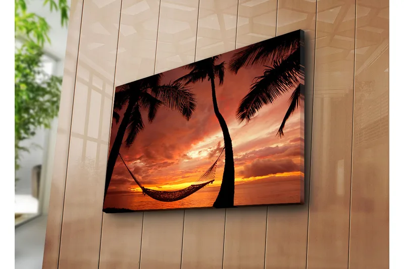 Canvas-taulu 70x45 cm - Auringonlasku meren yllä riippumatossa palmujen välissä, Oranssi / Musta / Punainen