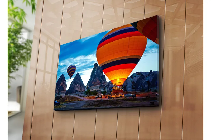 Canvas-taulu 70x45 cm - Värikkäät kuumailmapallot leijuvat dramaattisten kallioiden yllä kirkkaalla taivaalla, Oranssi / Sininen / Harmaa